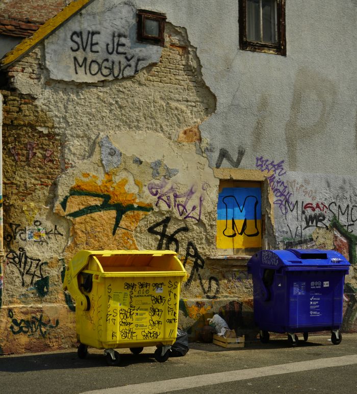 Vivid waste bins by a graffiti-covered wall in an urban alleyway in Zagreb, Croatia.