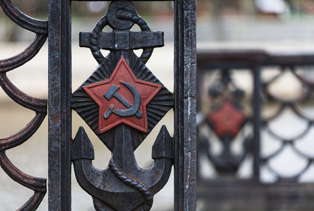 Close-up of an old iron fence featuring a Soviet anchor design with a red star and hammer and sickle symbol.